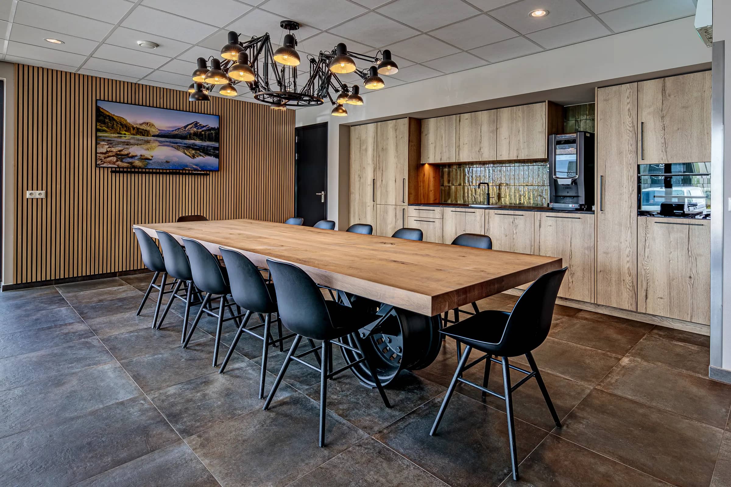 Canteen with a long light table on a truck wheel base, black chairs and a wooden slat wall at Van Wieren in Emmeloord